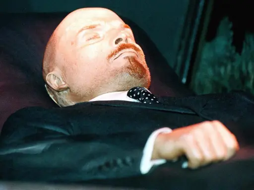 Mumia Lenina w garniturze i z krawatem w kropki, spoczywająca w szklanej gablocie.