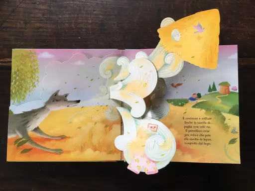 Libri pop-up più belli: un lupo soffia su una casetta di paglia, mentre un maialino corre verso una casetta di legno.