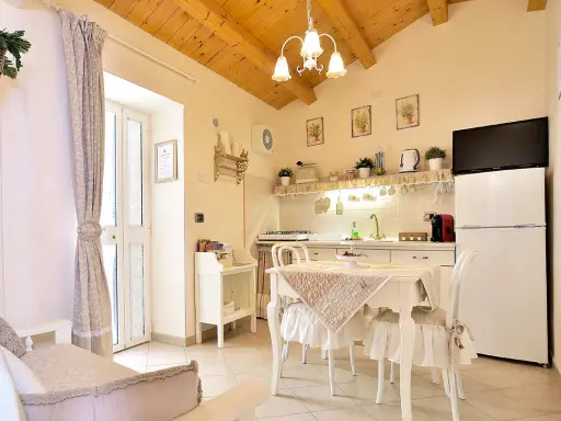 Cuisine et coin repas dans un style shabby chic, avec des meubles blancs, des textiles doux et des poutres apparentes.