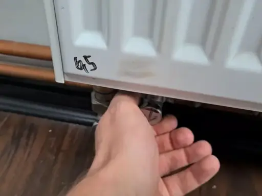 Ręka reguluje zawór grzejnika aluminiowego, próbując wyeliminować szum w grzejnikach aluminiowych.