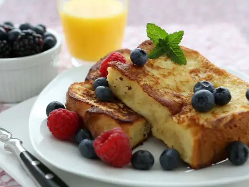 Deliciosa french toast receta, dorada y esponjosa, adornada con frambuesas, arándanos y menta. Un desayuno perfecto.