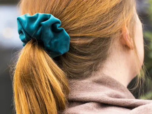 En hästsvans med en turkos scrunchie i sammet. Håret är kopparfärgat och faller mjukt.
