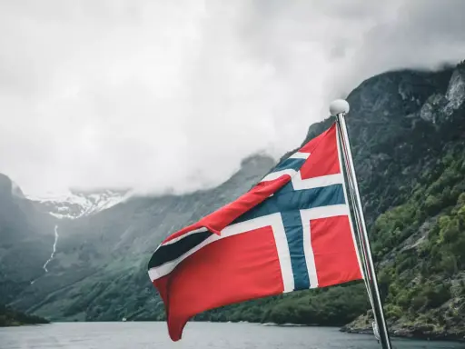 Norweska flaga na tle fiordu. Marzenie o pracy w Norwegii staje się rzeczywistością.