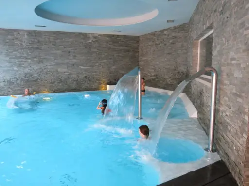 Bambini si divertono sotto cascate d'acqua in una piscina interna, un'ottima spa per famiglie in Lombardia.