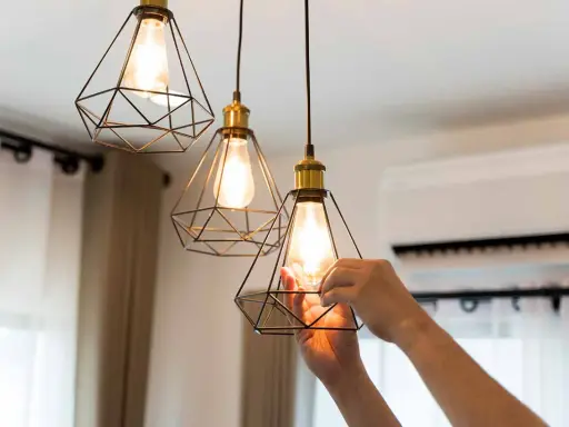 Man changing a lightbulb in a modern geometric pendant lamp, part of the simple home interiors.