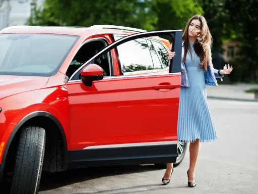 Mujer elegante sale de un monovolumen o SUV rojo brillante.