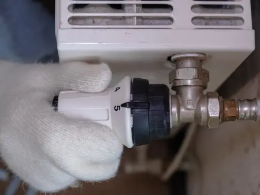 Main tenant ajuste le thermostat, réglant la température de son radiateur. Le raccord diélectrique montage est visible.