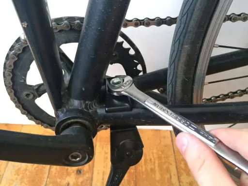 Montaż stopki rowerowej. Klucz dokręca śrubę mocującą stopkę do ramy roweru, obok korby i łańcucha.