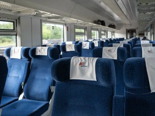 Puste niebieskie siedzenia w wagonie PKP Intercity z zagłówkami z logo.