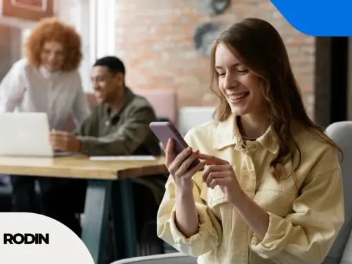 Uśmiechnięta kobieta korzysta z telefonu, podczas gdy koledzy pracują przy laptopie. To obraz skutecznego digital branding.
