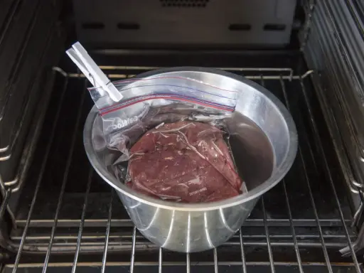 Vildsvinskött i vakuumpåse i en skål med vatten, redo för sous vide. Kontrollerar innertemp för perfekt resultat.
