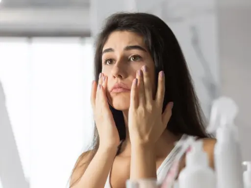 Donna preoccupata si tocca il viso, notando i segni dello stress sulla pelle.