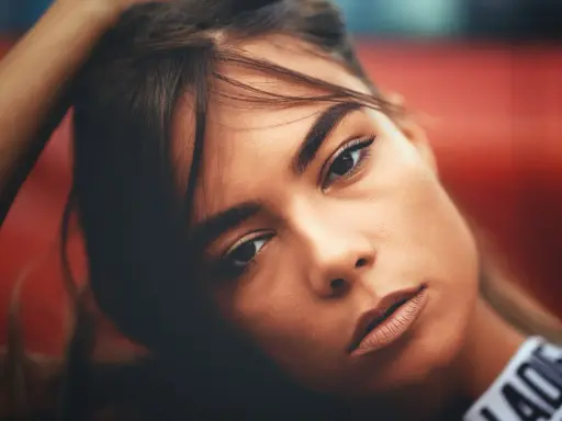 Portrait d'une jeune femme aux gros sourcils, la main dans les cheveux, regard intense.