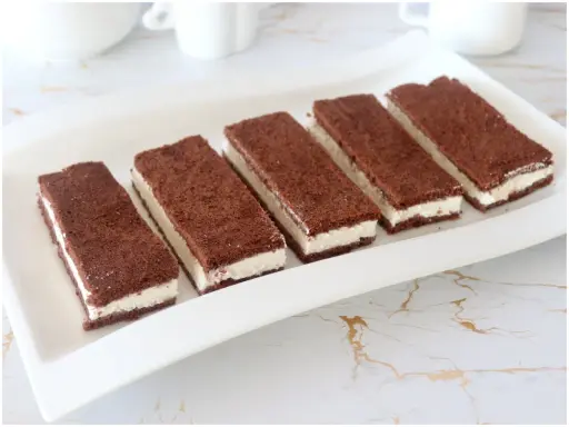 Sei fette di torta kinder fetta al latte, con pan di spagna al cacao e crema bianca, disposte su un piatto bianco.
