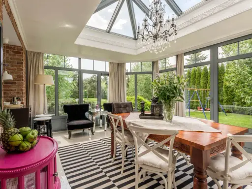 Une élégante verrière d'extension de maison baigne de lumière cette salle à manger, offrant une vue imprenable sur le jardin verdoyant.