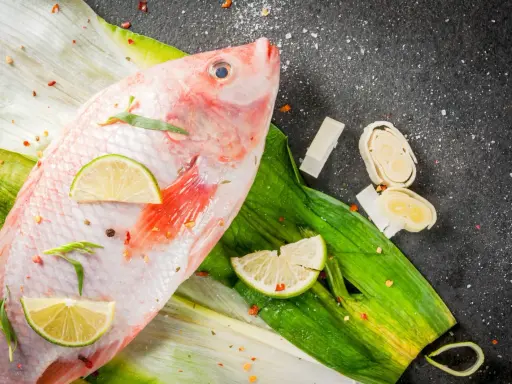 Cała ryba tilapia, przyprawiona chili i limonką, leży na zielonych liściach. Czy to tilapia, co to za ryba?