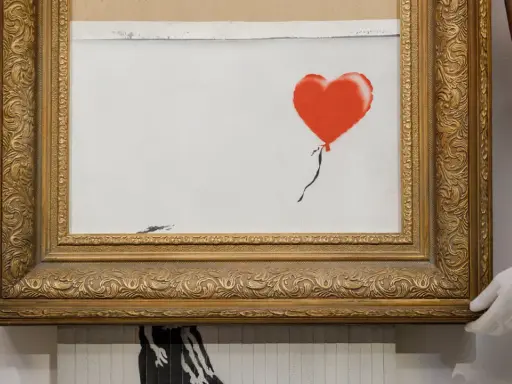 A framed Banksy artwork featuring a red balloon, hinting at how is Banksy rich.