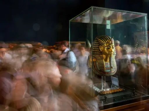 Goldene Maske des Pharao Tutanchamun in einer Vitrine, umgeben von verschwommenen Besuchern.