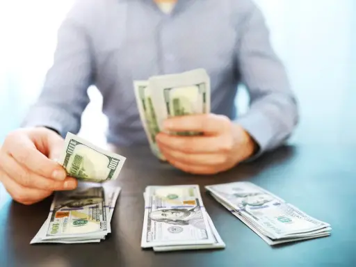 Mężczyzna liczy banknoty 100-dolarowe, symbolizujące dobrze płatne zawody i sukces finansowy.