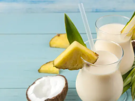 Dwa orzeźwiające koktajle pina colada z mlekiem, ozdobione kawałkami ananasa i liśćmi, na tle połówek kokosa.