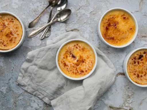Quatre crèmes brûlées dorées, prêtes à être dégustées. La croûte caramélisée de cette crème catalane invite à la gourmandise.