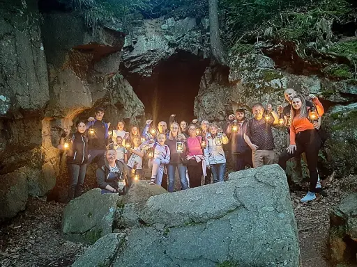 Grupa ludzi z latarniami przy skalnej grocie, odkrywająca tajemnice szlaku walońskiego.