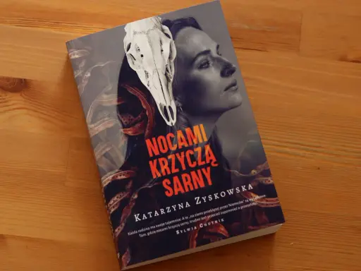 Okładka książki "Nocami krzyczą sarny" z czaszką sarny i twarzą kobiety. Tajemnicza historia o rodzinnych sekretach.