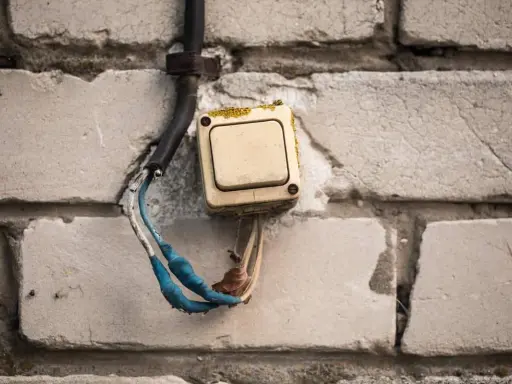 Interrupteur électrique beige en saillie sur un mur de briques, fils dénudés bleus et blancs.