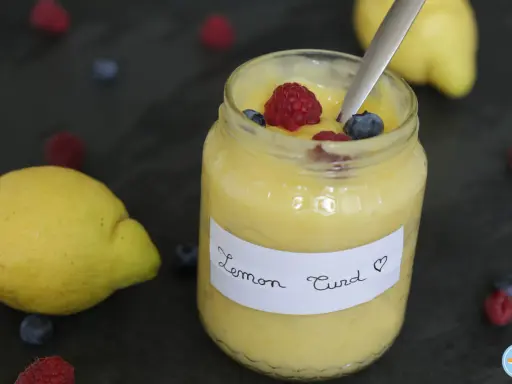 Un pot de lemon curd maison, garni de framboises et myrtilles, avec des citrons frais et des baies éparpillés.