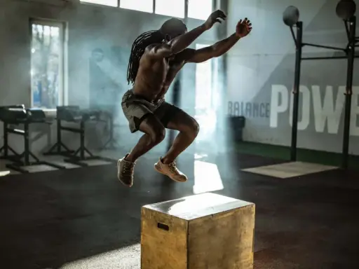 Mann mit Dreadlocks macht explosive Box Jumps in einem nebeligen Fitnessstudio.