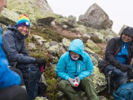 Vänner vilar på berg i snöfall, deras impregnerade jackor håller dem torra.