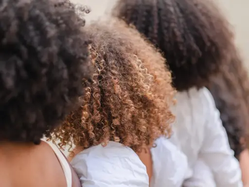 Trois femmes avec de magnifiques cheveux frisés, un mélange de bruns foncés et de châtain clair, se tiennent côte à côte.