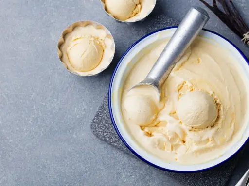 Glace vanille sorbetière crémeuse, servie dans un bol avec une cuillère à glace. Des gousses de vanille sont disposées à côté.