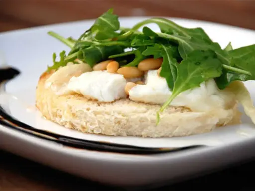 En bit rostat bröd med smält **chevre chaud**, pinjenötter och ruccola. En läcker förrätt.