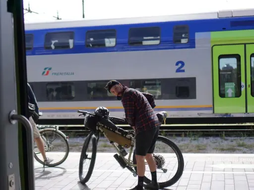 Ciclista con bici da gravel alla stazione, pronto per il viaggio da Rimini a Bellaria. Il treno Trenitalia è sullo sfondo.