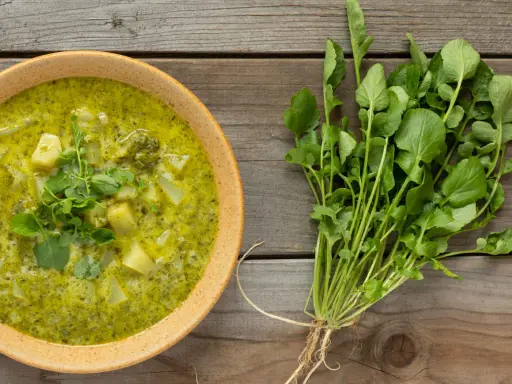 Soupe crémeuse aux pommes de terre et au cresson de para frais, garnie de feuilles vertes.