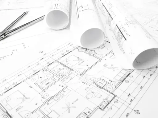 Projekt budowlany domu z widocznym cyrklem i zwiniętymi planami.