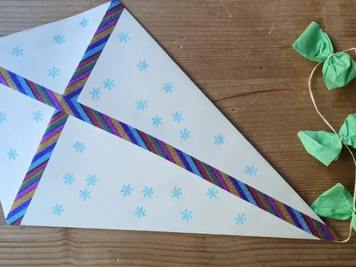 Ein selbstgebastelter Drachen mit Schneeflocken und bunten Bändern, perfekt für basteln mit Kindern ab 7 Jahre. Daneben eine Schnur mit grünen Schleifen und Holzperlen.