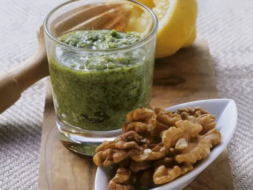 Frisches Petersilienpesto im Glas, daneben Walnüsse und eine Zitronenhälfte. Perfekt für Petersilie Rezepte.