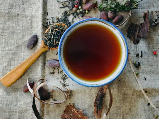 Une tasse de thé ambré, une cuillère de feuilles de thé, des fèves de cacao et des épices. Une invitation à découvrir les rooibos bienfaits.
