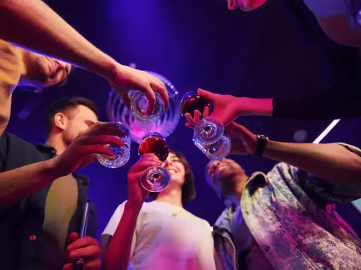 Grupa przyjaciół wznosi toast, świętując weekend. W tle dyskotekowe światła, sugerujące zabawę i być może początek weekendowego alkoholizmu.