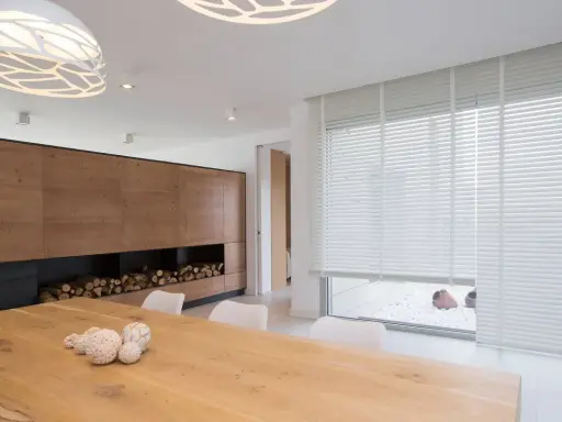 Un salon moderne avec un grand mur en bois, une table en bois et un type de store vénitien blanc qui habille une large fenêtre.