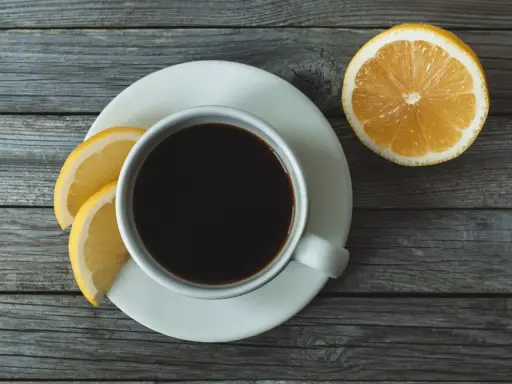 Eine Tasse schwarzer Kaffee mit Zitrone und Zitronenscheiben auf einem Holztisch.