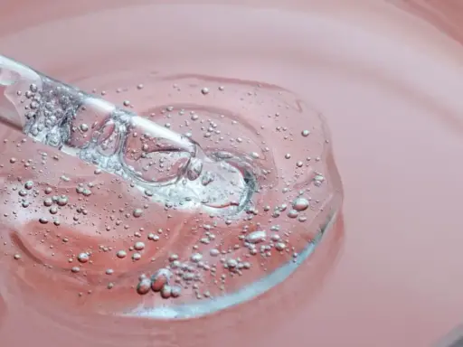 Goutte d'un sérum transparent avec des bulles, sur fond rose. C'est une illustration de ce que sont les peptides, des éléments clés pour la peau.