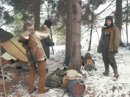 Zimowy obóz bushcraftowy. Dwie osoby w strojach z epoki, namiot, plecaki i sprzęt survivalowy.