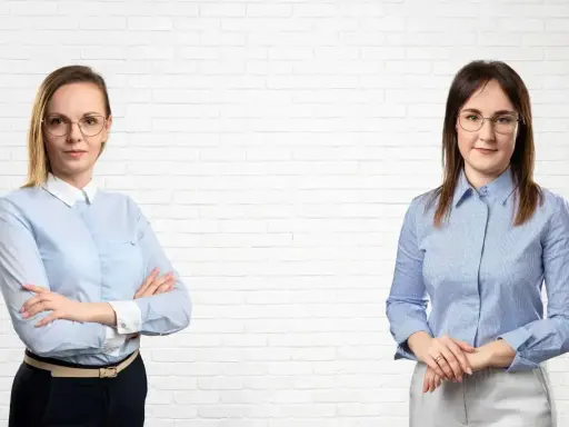 Dwie kobiety w koszulach stoją przed białą ceglaną ścianą.