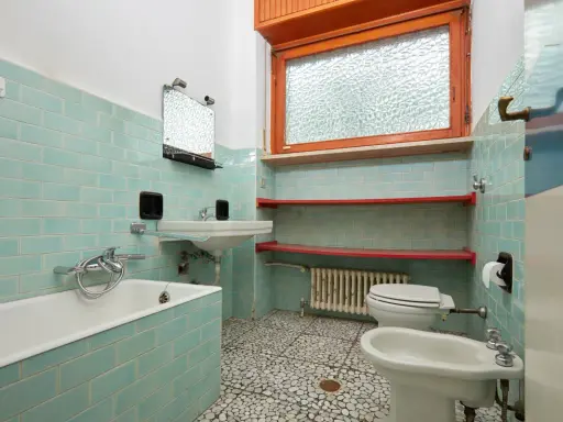 Bad renovieren ohne fliesen abschlagen: hellblau geflieste Wände, Badewanne, Waschbecken, Toilette, Bidet und Fenster.