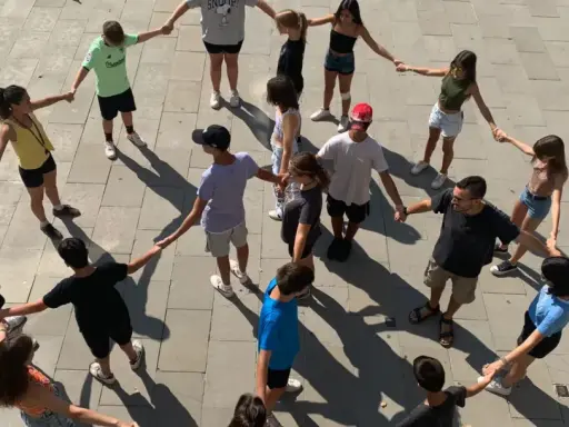 Un grupo de adolescentes participa en juegos cooperativos, tomados de la mano en un círculo en el exterior.