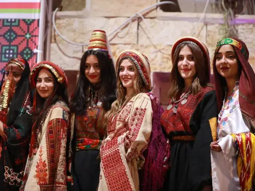 Six young women proudly showcase traditional Palestinian attire, highlighting the vibrant artistry of Palestinian designers.