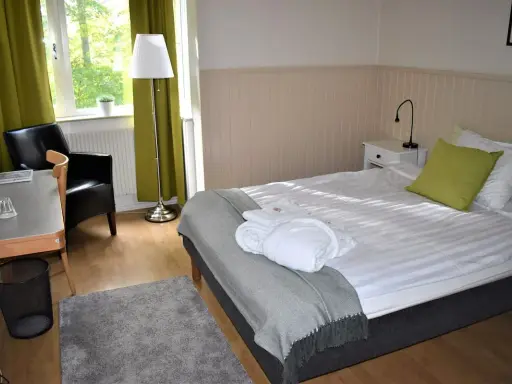 Ett mysigt rum på Wendelsbergs Hotell & Vandrarhem med en bekväm säng, fåtölj och skrivbord.